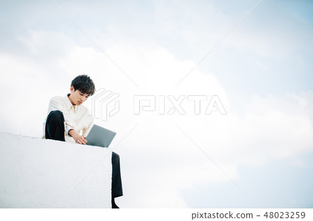 一個男人坐在屋頂上,打開一台筆記本電腦 一個男人坐在屋頂上,打開一台筆記本電腦 48023259