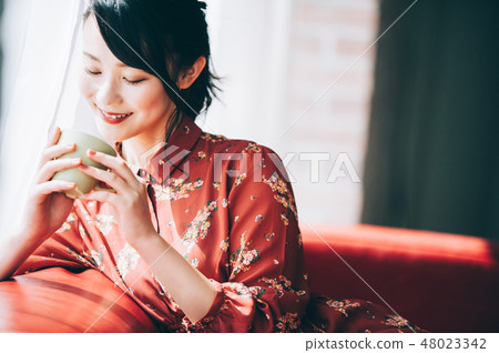 A red one-piece lady who uploaded her hair sitting on the sofa by the window 48023342