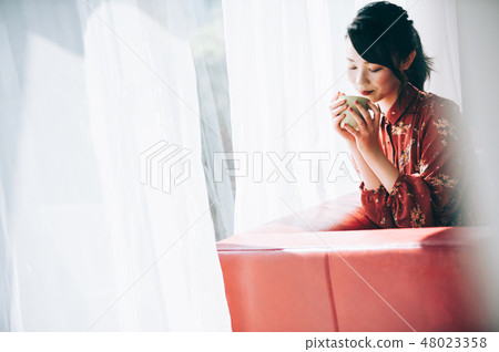 A red one-piece lady who uploaded her hair sitting on the sofa by the window 48023358