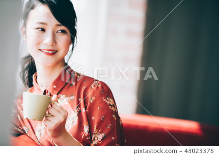 A red one-piece lady who uploaded her hair sitting on the sofa by the window 48023378
