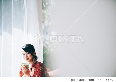 A red one-piece lady who uploaded her hair sitting on the sofa by the window 48023379