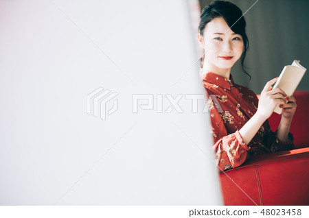 Sitting on a sofa on the window, reading a book A red one-piece lady who ups her hair 48023458