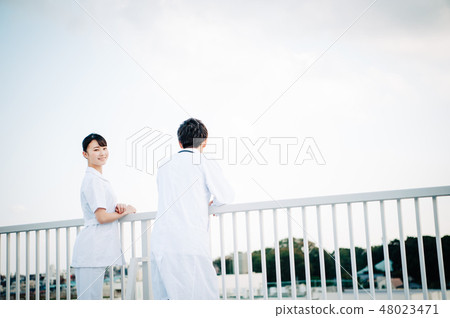 Men and women wearing white coats on the railing on the roof 48023471
