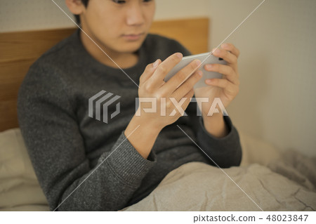 Boy using smartphone in bed Lack of sleep Junior high school student High school student body part Parts cut No face Boy using smartphone in bed Lack of sleep Junior high school student High school student body part Parts cut No face 48023847