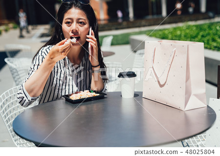 asian woman talking on smart phone eating salad 48025804