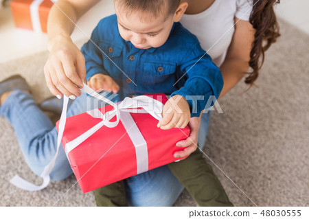 Present, children, birthday and holiday concept - little child boy unpacking gift box with mom Present, children, birthday and holiday concept - little child boy unpacking gift box with mom 48030555