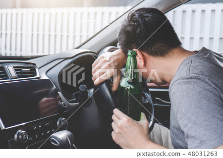 Young asian man drives a car with drunk a bottle of beer and fal Young asian man drives a car with drunk a bottle of beer and fal 48031263