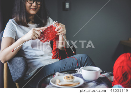 Close up shot of young woman hands knitting a red scarf handicra 48031549
