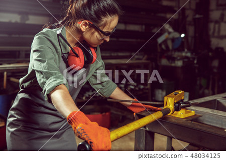 Busy and serious craftswoman grinding timbers with special machine. 48034125