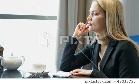 Young blonde girl doing homework, writing notes in notepad sitting in cafe Young blonde girl doing homework, writing notes in notepad sitting in cafe 48035753