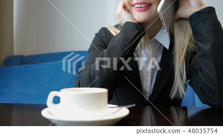 unrecognizable smiling young woman having friendly phone conversation while drinking coffee in cafe. unrecognizable smiling young woman having friendly phone conversation while drinking coffee in cafe. 48035754