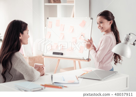 Clever schoolgirl pointing on a whiteboard standing in front of mother Clever schoolgirl pointing on a whiteboard standing in front of mother 48037911