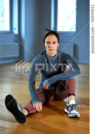 beautiful fit woman in sportswear posing while sitting on the floor in front of window at gym 48044031