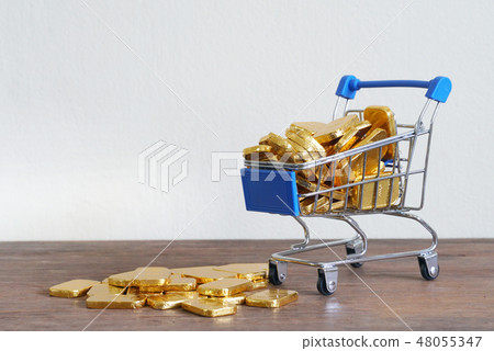 Gold bars spill out from shopping cart on table Gold bars spill out from shopping cart on table 48055347