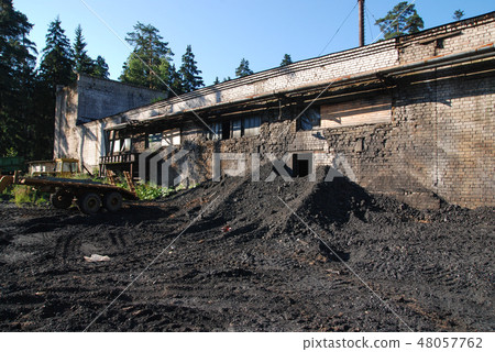 Pile of black coal pieces near the dirt gray brick wall of a building in the forest Pile of black coal pieces near the dirt gray brick wall of a building in the forest 48057762