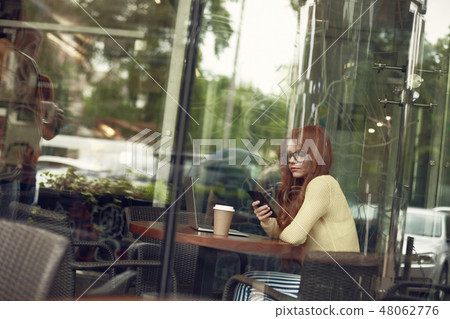 Beautiful young lady with hot drink using cellphone in cozy cafe 48062776