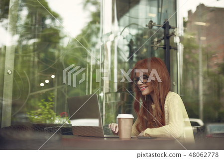 Cheerful pretty girl with hot drink using laptop in cozy cafe Cheerful pretty girl with hot drink using laptop in cozy cafe 48062778