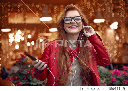 Attractive red-haired girl listening music on smartphone 48063149