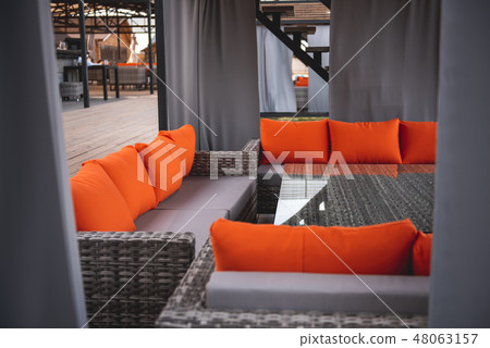 Comfortable terrace of the outdoors cafe with orange pillows on couches Comfortable terrace of the outdoors cafe with orange pillows on couches 48063157