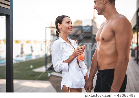 Shirtless man standing with his smiling girlfriend and holding her hand Shirtless man standing with his smiling girlfriend and holding her hand 48063492