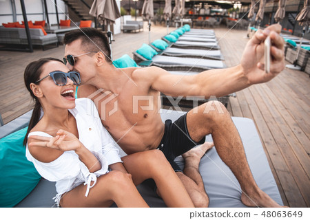 Shirtless man kissing his girlfriend while taking selfie 48063649
