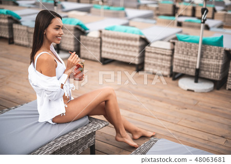 Full length of pretty woman sitting on the lounge sun chair with her cocktail 48063681