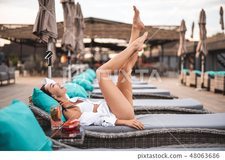 Happy woman putting legs up while lying on the lounge sun chair 48063686