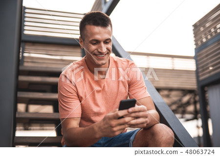 Happy man sitting on the stairs and using his smartphone Happy man sitting on the stairs and using his smartphone 48063724