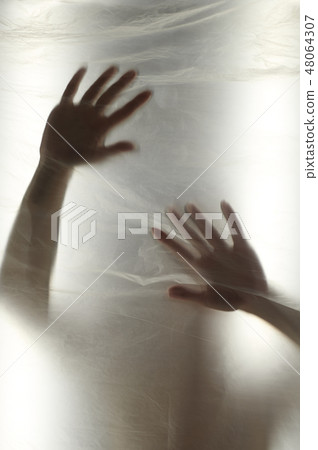 Hands through the clear film.Beautiful delicate feminine hands. A symbol of illusiveness and 48064307