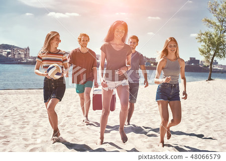 Friends on the beach. Rear view of cheerful young people walking by the beach to the sea while two Friends on the beach. Rear view of cheerful young people walking by the beach to the sea while two 48066579