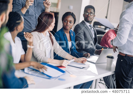 Mixed race people listening to presentation sitting in row at boardroom table 48075711