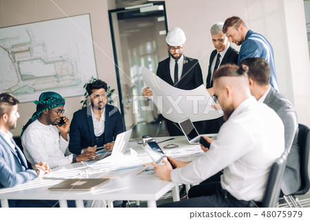 Multiracial group of constructors and architects discussing blueprint at office. Multiracial group of constructors and architects discussing blueprint at office. 48075979
