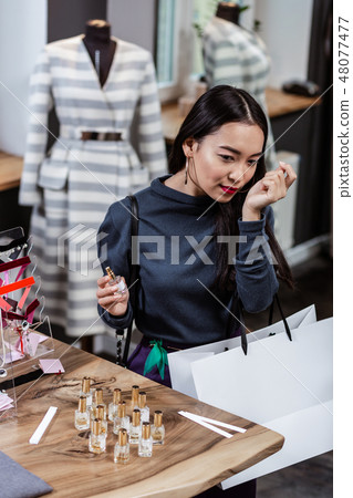Long-haired cute lady in a white sweater choosing a perfume Long-haired cute lady in a white sweater choosing a perfume 48077477