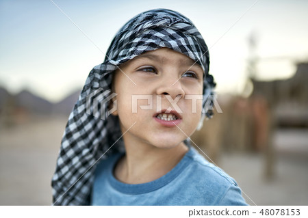 Small boy in checkered keffiyeh grimacing outdoors 48078153