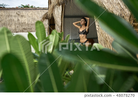 Brunette woman in sexy dark lingerie posing in bungalow at tropical resort 48078270