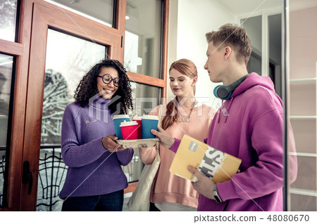Curly student wearing glasses bringing coffee for her friends 48080670