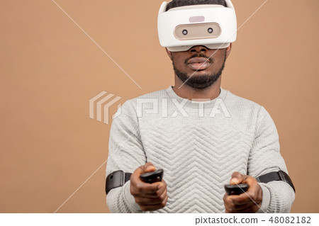 Black man wearing 3d vr glasses, playing videogame, holding joystick in hands Black man wearing 3d vr glasses, playing videogame, holding joystick in hands 48082182