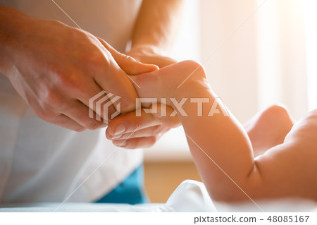 Masseur does foot massage for small child lying on stomach. Masseur does foot massage for small child lying on stomach. 48085167