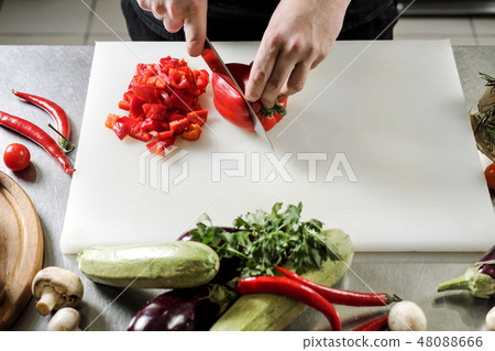 Male chef cuts vegetables for salad in a restaurant in a black apron. White cutting board, closeup Male chef cuts vegetables for salad in a restaurant in a black apron. White cutting board, closeup 48088666