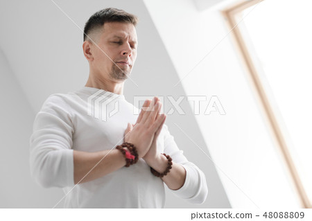 A man in white clothes on a white background with his hands folded on his chest. Meditation and 48088809