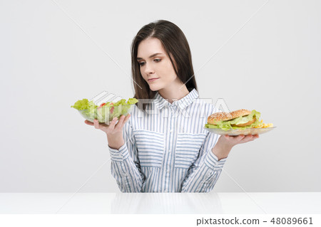 Slender brunette girl on a white background chooses between a plate of fast food and hamburgers and 48089661