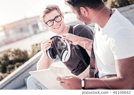 Positive student taking headphones from his friend 48100682