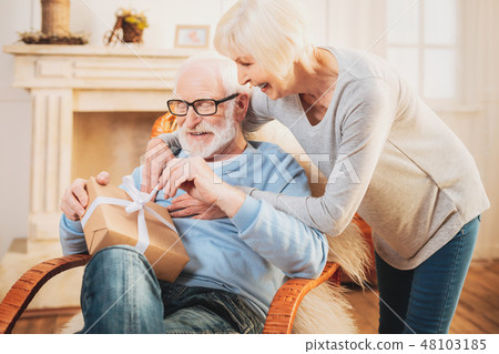Caring wife helping her smiling man unpacking present Caring wife helping her smiling man unpacking present 48103185