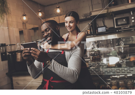 Beautiful girl barista hugs a man holding a tablet Beautiful girl barista hugs a man holding a tablet 48103879