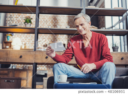 Calm senior person kindly smiling while dealing with bills Calm senior person kindly smiling while dealing with bills 48106931