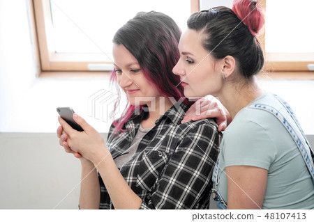 Couple of beautiful young girls in a room with white walls by the window. Communicate and write on Couple of beautiful young girls in a room with white walls by the window. Communicate and write on 48107413