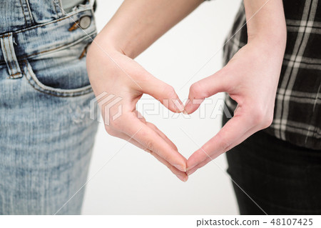 Two girls in jeans hold hands close up. White background. Homosexual lesbian couple. Two girls in jeans hold hands close up. White background. Homosexual lesbian couple. 48107425