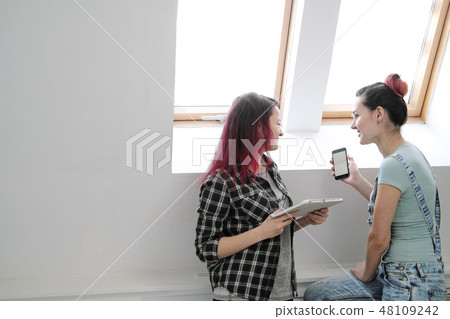Couple of beautiful young girls in a room with white walls by the window. Communicate and write on Couple of beautiful young girls in a room with white walls by the window. Communicate and write on 48109242