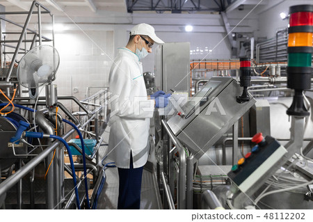 Technologist stands with a tablet near the digital screen at the dairy Plant Technologist stands with a tablet near the digital screen at the dairy Plant 48112202
