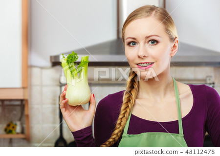 Woman in kitchen holds raw fennel bulb vegetable 48112478
